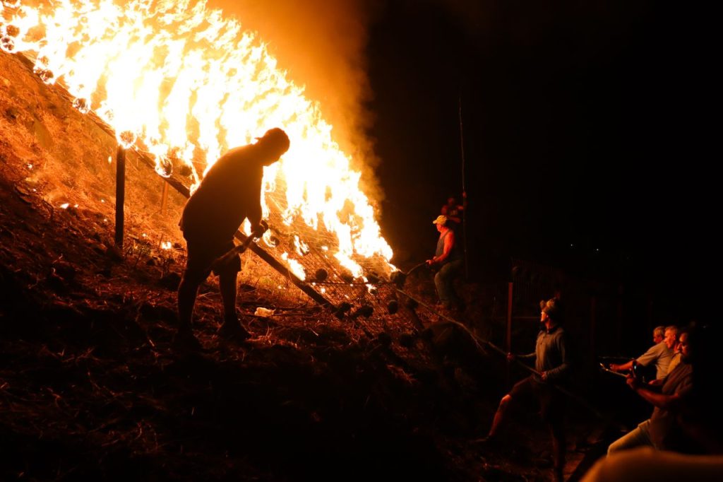 Dramatic scene of firefighters combating a fierce fire on a hillside at night.